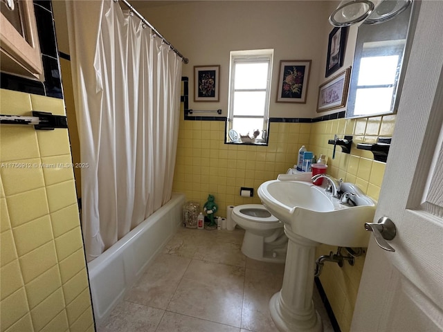 full bath featuring tile walls, shower / bathtub combination with curtain, toilet, wainscoting, and tile patterned flooring