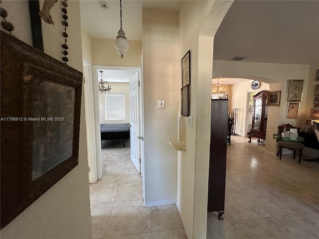 hallway with arched walkways, visible vents, baseboards, and an inviting chandelier