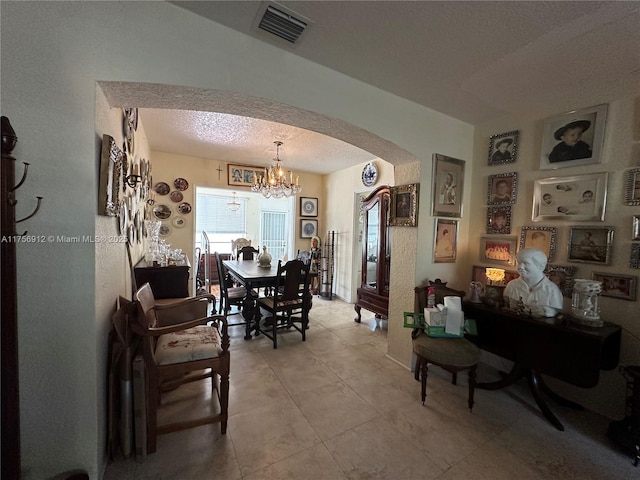 dining room featuring arched walkways, a textured ceiling, light tile patterned flooring, visible vents, and an inviting chandelier