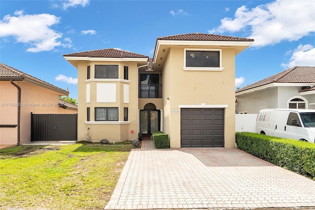 mediterranean / spanish house featuring decorative driveway, a tile roof, stucco siding, fence, and a balcony