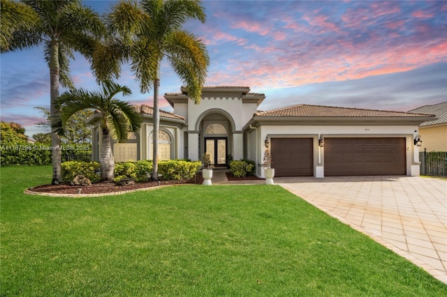 mediterranean / spanish house with french doors, decorative driveway, stucco siding, a front yard, and a garage