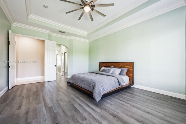 bedroom featuring visible vents, arched walkways, a raised ceiling, and wood finished floors