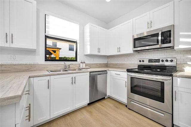 kitchen with a sink, stainless steel appliances, white cabinets, and light wood finished floors