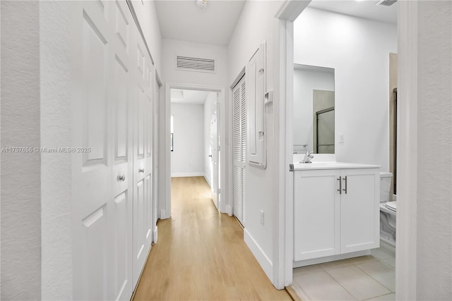 hall featuring baseboards, visible vents, and light wood finished floors