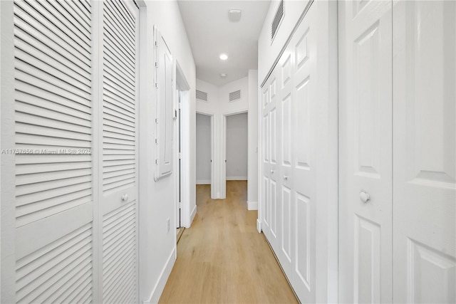 corridor with light wood-type flooring, visible vents, and baseboards