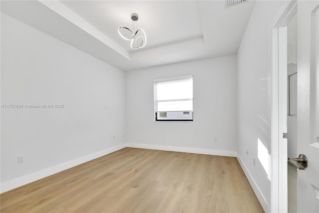 spare room featuring visible vents, baseboards, light wood-type flooring, a tray ceiling, and a notable chandelier