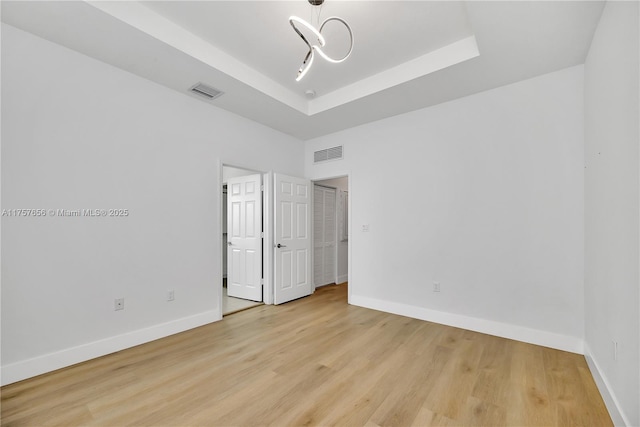 spare room featuring a raised ceiling, light wood-style flooring, baseboards, and visible vents