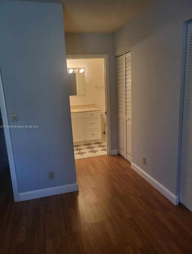 unfurnished bedroom with a textured ceiling, ensuite bathroom, wood finished floors, and baseboards