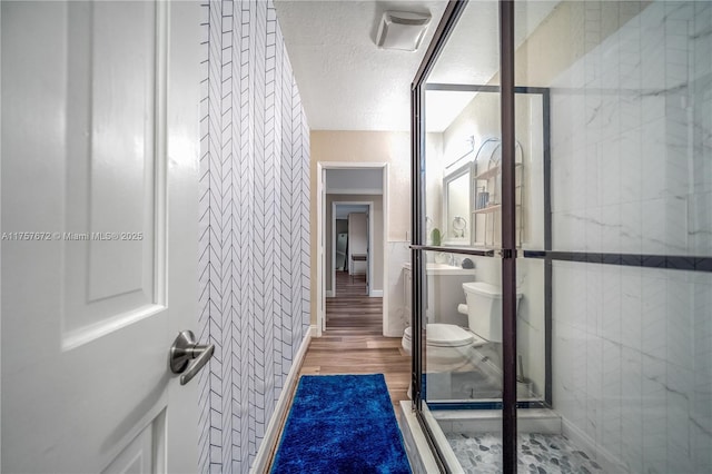 bathroom featuring tile walls, toilet, a shower stall, a textured ceiling, and wood finished floors