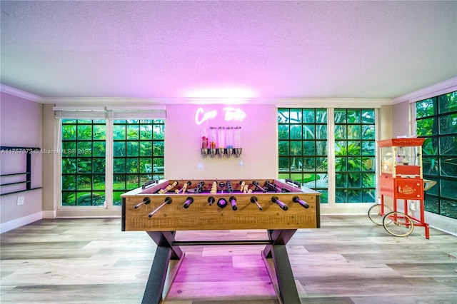 recreation room featuring ornamental molding, a textured ceiling, baseboards, and wood finished floors