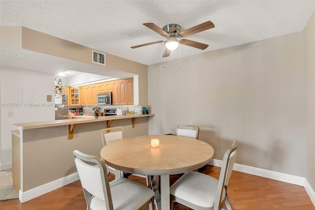 dining room with a textured ceiling, baseboards, visible vents, and light wood-style floors