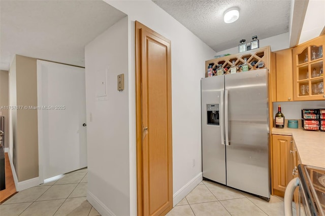 kitchen featuring light tile patterned floors, stainless steel appliances, light countertops, glass insert cabinets, and a textured ceiling