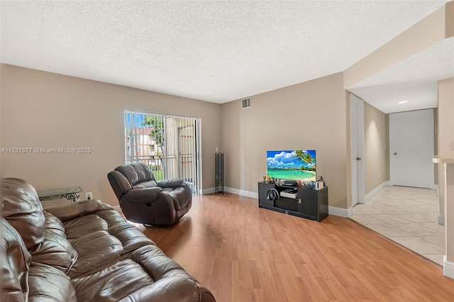 living area with light wood-type flooring, baseboards, visible vents, and a textured ceiling