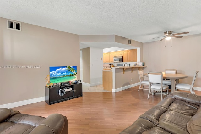 living area featuring light wood-type flooring, visible vents, ceiling fan, and a textured ceiling