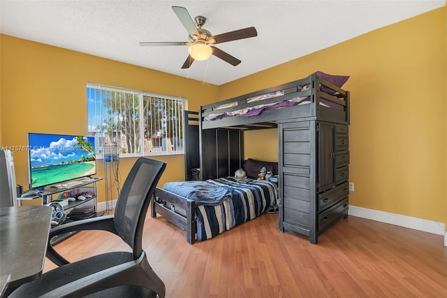 bedroom with light wood-style flooring, a textured ceiling, baseboards, and a ceiling fan