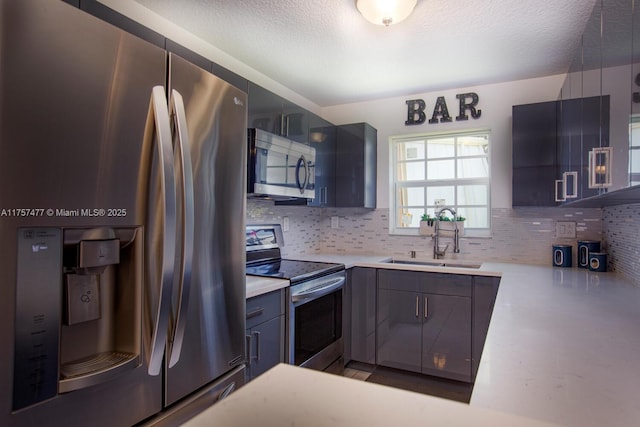 kitchen with a textured ceiling, stainless steel appliances, a sink, light countertops, and tasteful backsplash