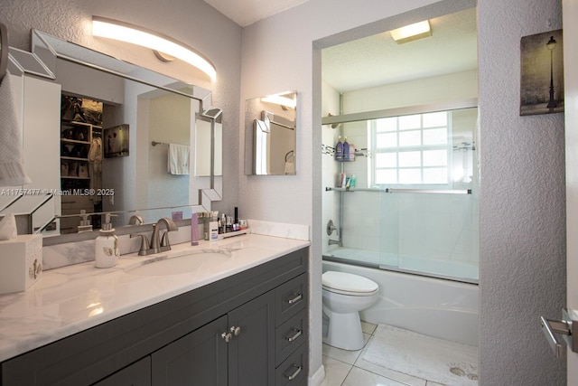 bathroom with a textured wall, bath / shower combo with glass door, vanity, and toilet