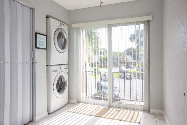 washroom with laundry area, baseboards, stacked washer / dryer, a textured wall, and light tile patterned flooring