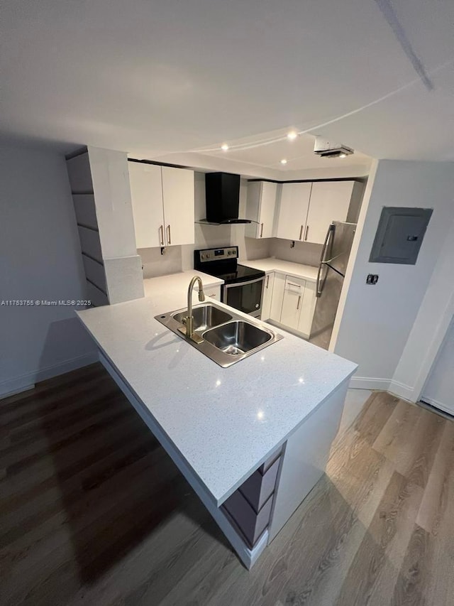 kitchen featuring stainless steel appliances, a sink, wall chimney range hood, electric panel, and a peninsula