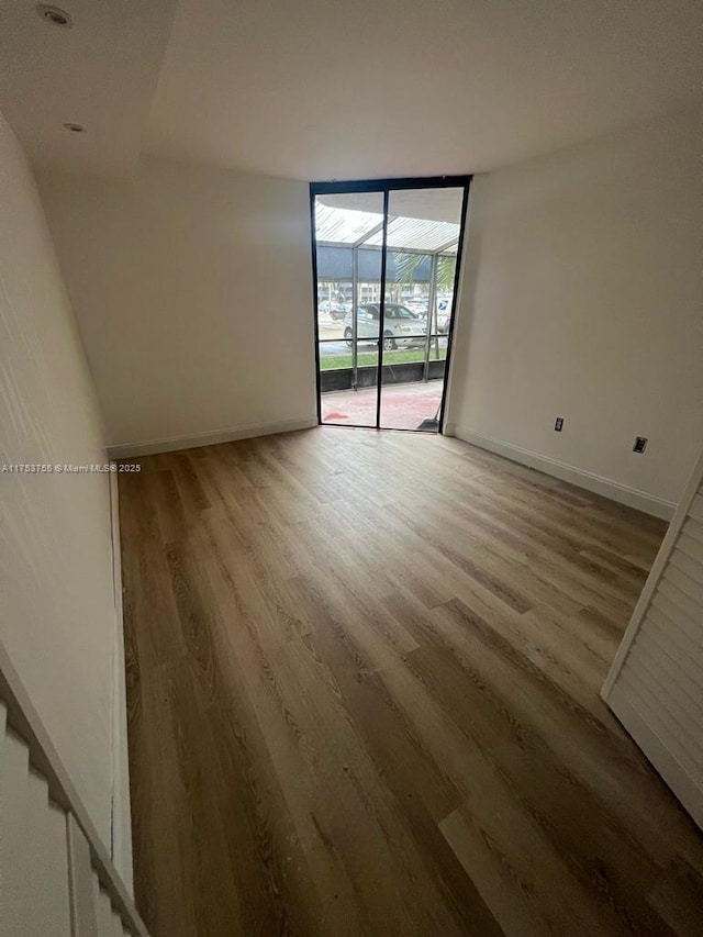 empty room featuring expansive windows, wood finished floors, and baseboards