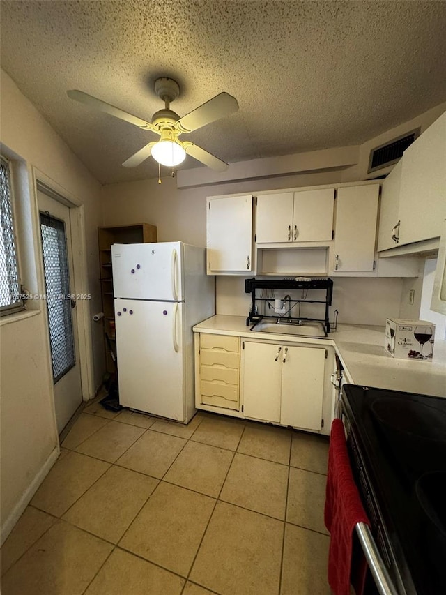 kitchen with light tile patterned floors, visible vents, freestanding refrigerator, light countertops, and a sink