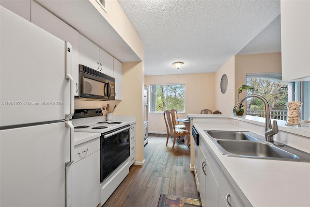 kitchen with white appliances, white cabinets, dark wood-style flooring, light countertops, and a sink