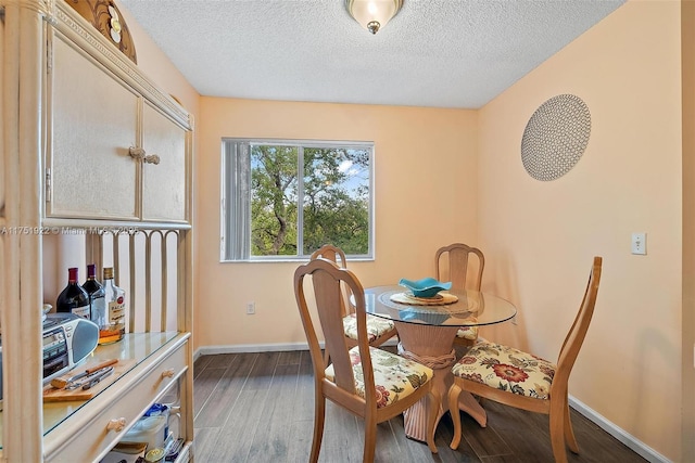 dining space with a textured ceiling, baseboards, and wood finished floors