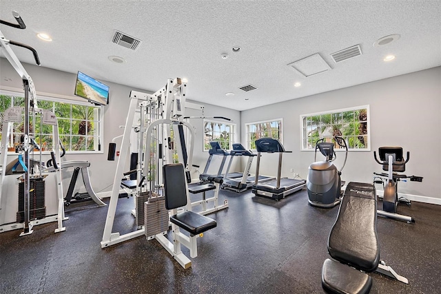 gym featuring a textured ceiling, visible vents, and a healthy amount of sunlight