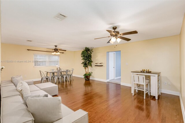 living room with visible vents, ceiling fan, baseboards, and wood finished floors