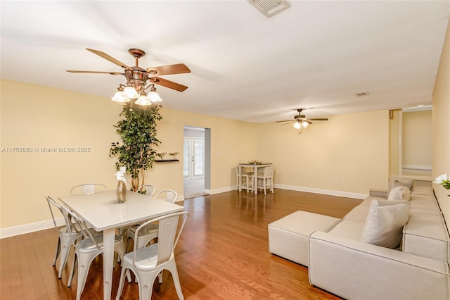 living area featuring baseboards, wood finished floors, visible vents, and ceiling fan