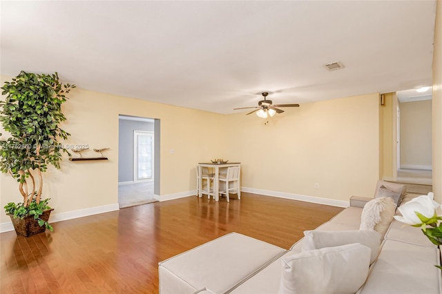 living area with a ceiling fan, wood finished floors, visible vents, and baseboards