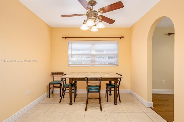 tiled dining space with baseboards, arched walkways, and a ceiling fan