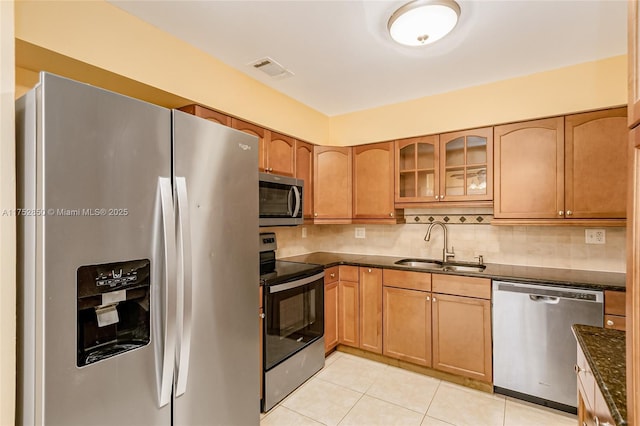 kitchen with stainless steel appliances, backsplash, light tile patterned floors, a sink, and glass insert cabinets