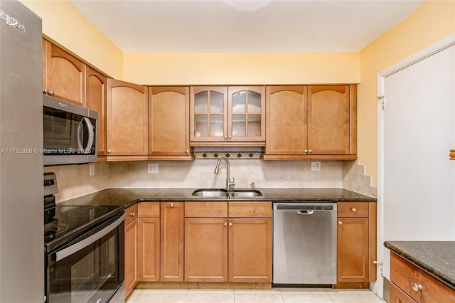 kitchen with a sink, appliances with stainless steel finishes, decorative backsplash, dark stone counters, and glass insert cabinets