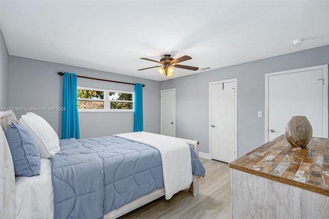 bedroom featuring light wood-type flooring, visible vents, baseboards, and ceiling fan