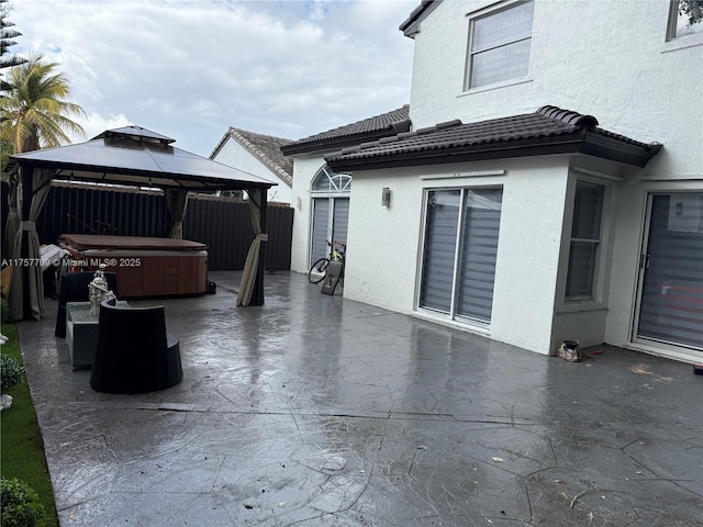 view of patio / terrace featuring a hot tub, fence, and a gazebo