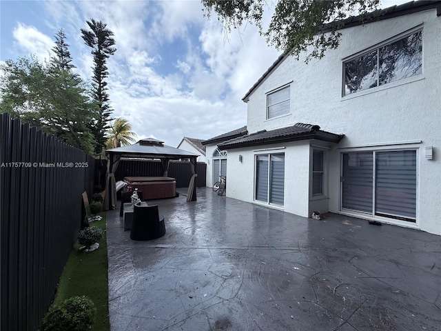 exterior space featuring a hot tub, a fenced backyard, a gazebo, a patio area, and stucco siding