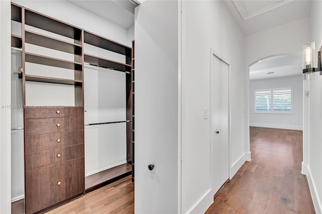 hallway with arched walkways, baseboards, and wood finished floors