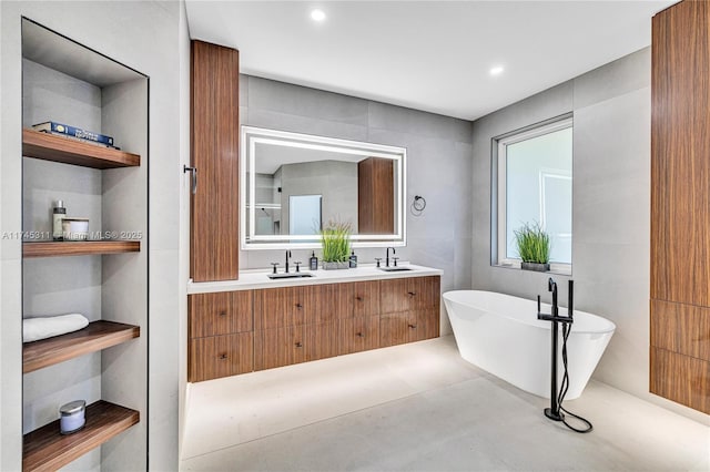 full bath with a soaking tub, double vanity, tile walls, and a sink