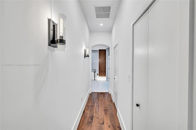 hall featuring visible vents, arched walkways, baseboards, and dark wood-style flooring