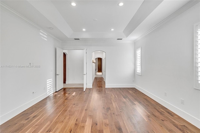 spare room with light wood-type flooring, arched walkways, a raised ceiling, and baseboards