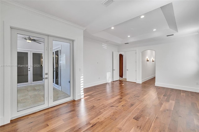 empty room featuring visible vents, a tray ceiling, arched walkways, light wood-style floors, and french doors