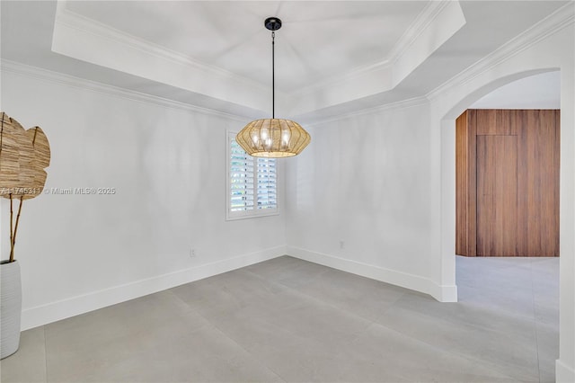 unfurnished dining area with baseboards, a tray ceiling, ornamental molding, arched walkways, and a notable chandelier