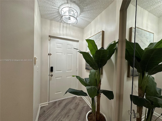 entryway featuring an inviting chandelier, baseboards, a textured ceiling, and wood finished floors