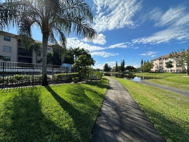 surrounding community with a water view, fence, and a lawn