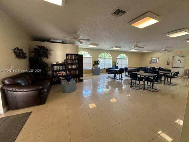 living area with a ceiling fan, visible vents, a textured ceiling, and light tile patterned flooring