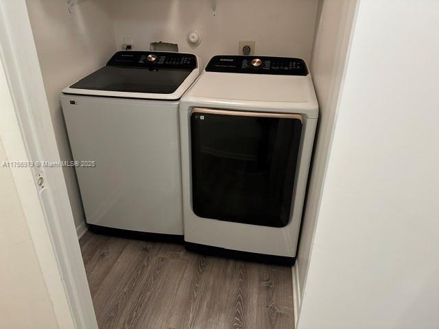 clothes washing area with laundry area, washing machine and dryer, and wood finished floors