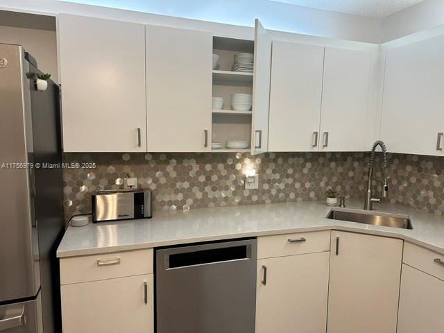 kitchen featuring stainless steel appliances, a sink, white cabinets, light countertops, and decorative backsplash