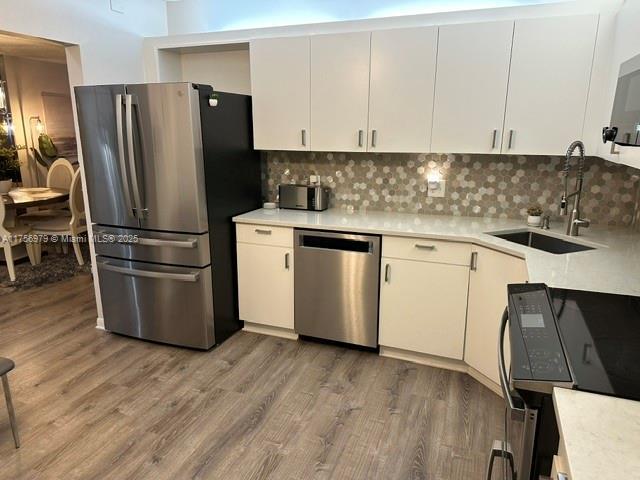 kitchen featuring tasteful backsplash, light countertops, appliances with stainless steel finishes, a sink, and wood finished floors