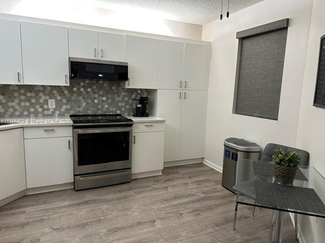 kitchen with light wood-style flooring, electric stove, light countertops, and a textured ceiling